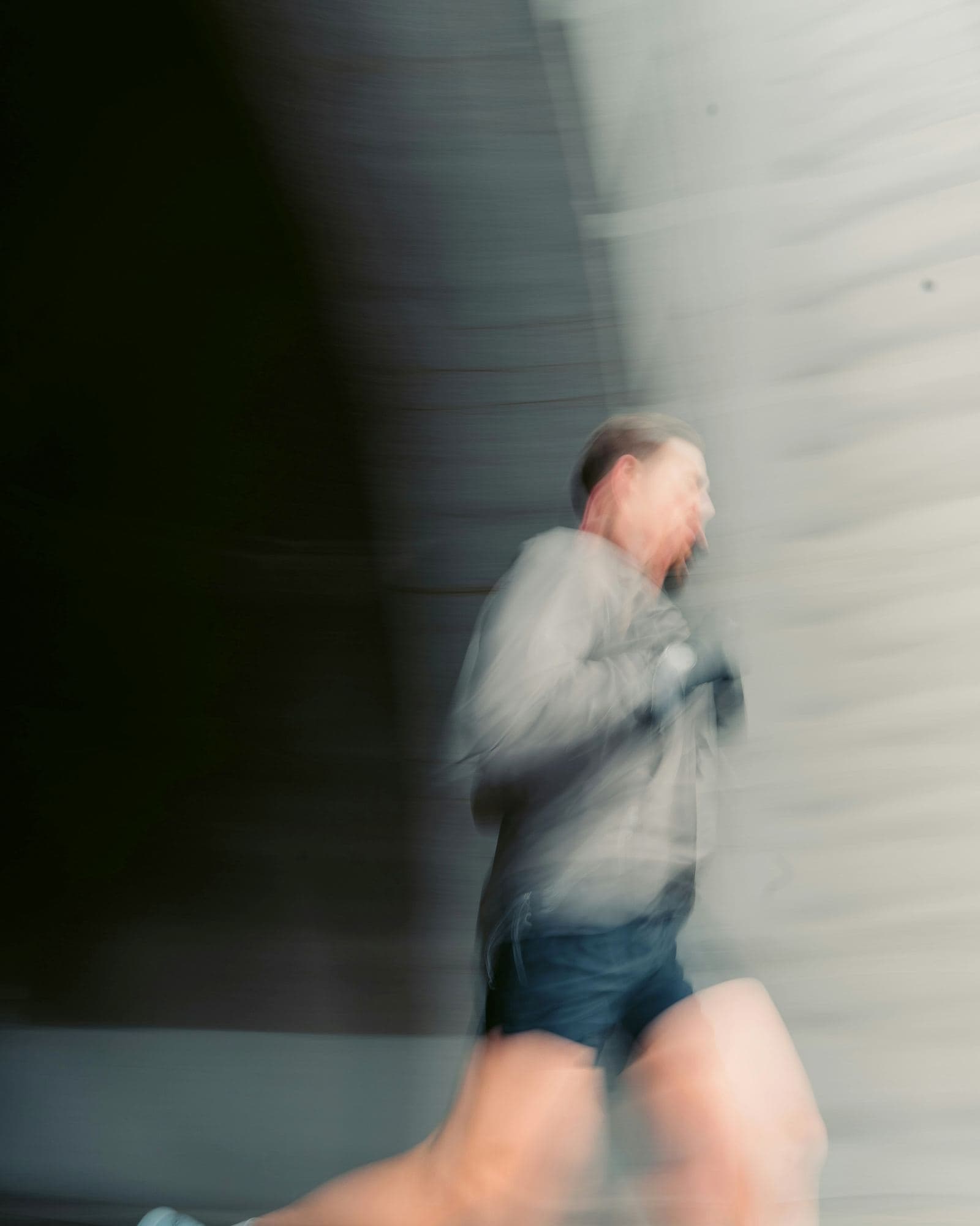 A runner captured with a long exposure, blurred with forward motion against a pale wall.